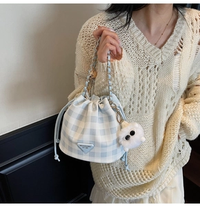 Detail der blau karierten Beuteltasche mit Plüsch-Anhänger und Kettengurt am Modell
