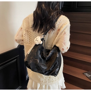 Dettaglio della borsa hobo nera lucida con ciondolo a forma di orso sulla spalla della modella