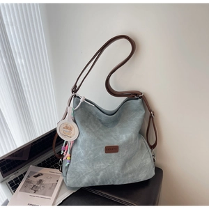 Close-up of light blue textured tote bag with brown straps and cute Capybara charm