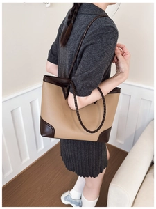 Detail of contrast-colored leather tote bag featuring woven straps and reinforced base
