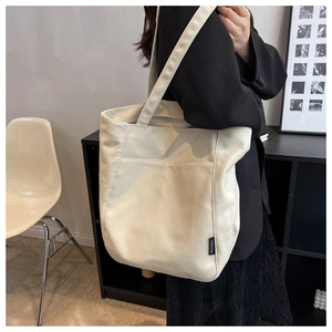 Detail of a large off-white canvas tote bag featuring a brand woven label and wide shoulder strap