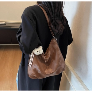 Dettaglio di una grande borsa hobo marrone in pelle lucida con ciondolo a orsetto