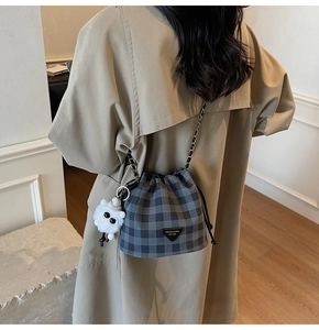 Detail der grauen karierten Beuteltasche mit Plüschanhänger an einem beigen Trenchcoat
