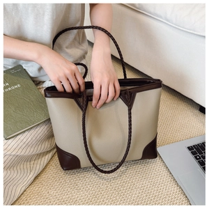 Detail of beige lychee texture tote with dark brown edges and hand-woven handle on sofa