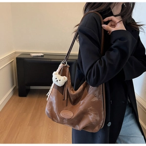 Dettaglio borsa hobo marrone in pelle cerata con ciondolo a forma di orsetto bianco