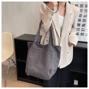 Detail of grey canvas tote bag with side label and vertical stitching on model
