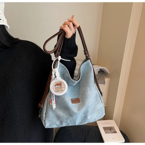 Detail of teal canvas tote bag with Capybara charm and brand leather logo patch