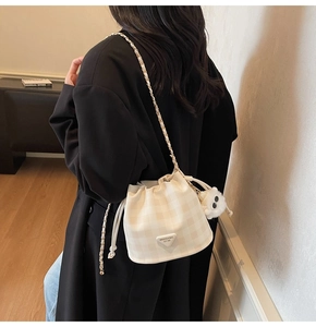 Detail der beigen karierten Kordelzug-Beuteltasche mit Kettenriemen und Lamm-Anhänger