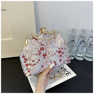 Detailed embroidery of red plum blossoms on a purple silk evening bag with metal handle
