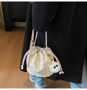 Detail der cremeweißen Beuteltasche mit Schachbrettmuster und Plüschmonster-Anhänger