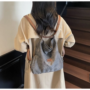 Rear view of a grey canvas backpack with brown leather straps on a wooden staircase
