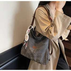 Detail of dark grey tote bag with brown leather straps and colorful bead pendant