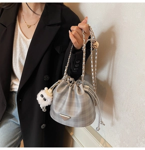 Detail der silbernen Karo-Beuteltasche mit Kettenriemen und Plüschmonster-Anhänger
