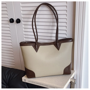 Detail of the woven handle and leather texture on a beige and brown tote bag