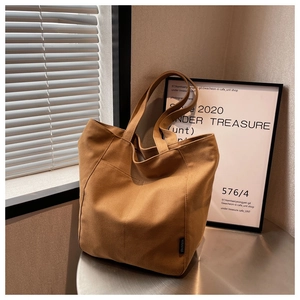 Detail of a brown canvas tote bag featuring structural stitching and brand woven label