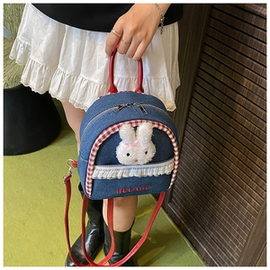Detail of denim mini backpack featuring plush rabbit, lace trim and red handles