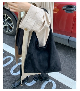 Close-up of black suede tote bag with wide shoulder strap worn by a person outdoors