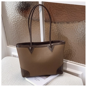 Detail of a brown pebbled leather tote featuring woven handles and reinforced corners