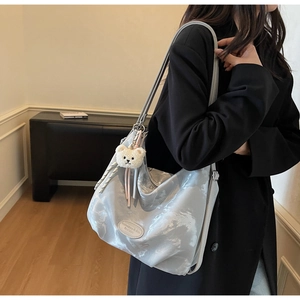 Dettaglio della borsa a tracolla plissettata argento con ciondolo a orsetto e logo in pelle