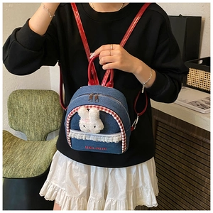 Detail of denim mini backpack with plush bunny, lace trim, and red embroidery