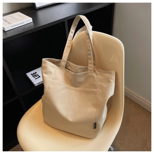 Detail of the cream canvas tote bag showing the side pocket and wide shoulder straps