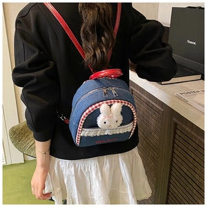 Detail of denim backpack with cute plush bunny, lace trim and contrast red leather straps