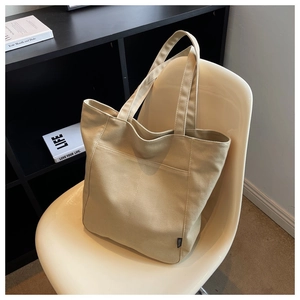 Large beige canvas tote bag with front pocket displayed on a modern minimalist chair