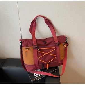 Détail du sac de voyage bordeaux avec cordons élastiques orange et bandoulière