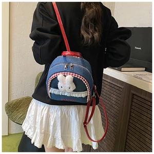 Detail of denim mini backpack with plush rabbit, red straps, and lace trim on model
