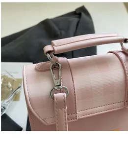 Dettaglio del gancio in metallo e manico in pelle rosa su borsa a mano a quadretti