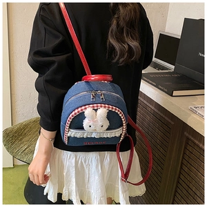 Detail view of denim mini backpack with plush rabbit decor and red leather handles