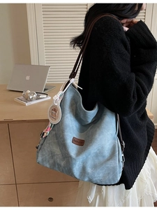 Light blue canvas tote bag with leather logo and charms shown in a home office setting