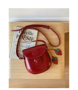 Detail of red leather saddle bag with strawberry charms and embossed logo