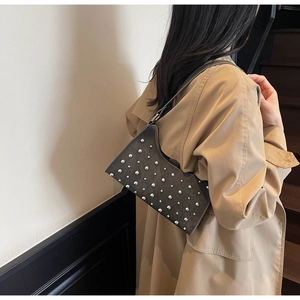 Détail d'un sac baguette en daim gris foncé avec clous porté sur un trench-coat