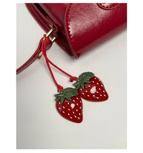 Detail of red faux leather saddle bag featuring two cute strawberry charms with gold hardware