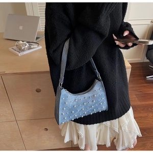 Détail du sac sous le bras en denim bleu clair avec clous argentés et fermeture éclair