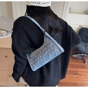 Gros plan du sac sous le bras en denim bleu clair orné de rivets argentés sur l'épaule