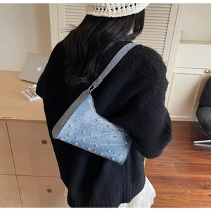 Gros plan d'un sac à bandoulière bleu clair orné de rivets porté par un mannequin