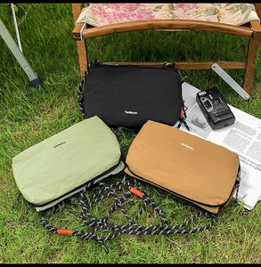 Three minimalist nylon crossbody bags in black, green, and brown on a wooden chair