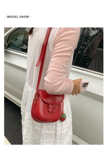 Detail of red leather saddle bag with strawberry charm and embossed logo on the flap