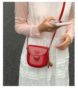 Close-up of red retro saddle bag with glossy finish and cute strawberry charm detail