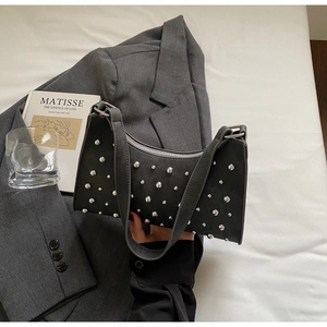 Détail du sac croissant gris foncé avec clous argentés et texture mate sur fond neutre