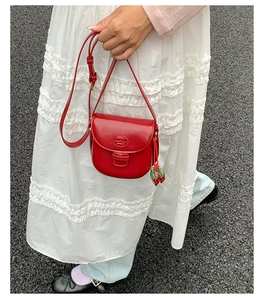 Detail of red leather mini saddle bag with strawberry charm and crossbody strap