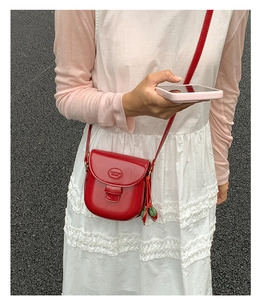 Detail of red mini saddle bag with strawberry charm and embossed logo on glossy finish