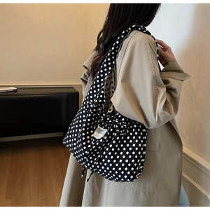 Detail of black polka dot canvas tote with bow tie worn with a beige trench coat