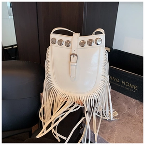 Detail of white glossy leather bucket bag featuring long fringe and silver rivets accents