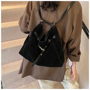 Close-up of black faux suede backpack with golden hardware on a model in a brown coat
