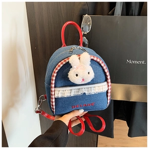 Detail of denim mini backpack featuring plush rabbit, lace trim, and red leather straps