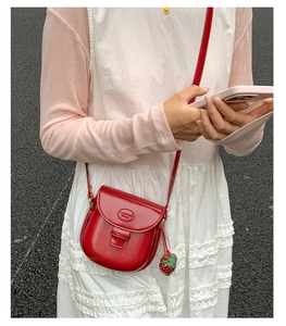 Detailed side view of a red saddle bag with strawberry charm worn by a model