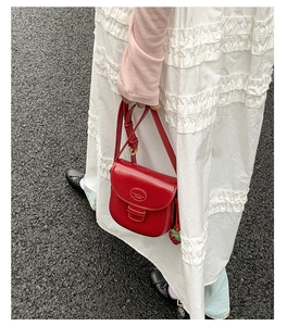 Detail of red vintage saddle bag with strawberry charm and adjustable strap